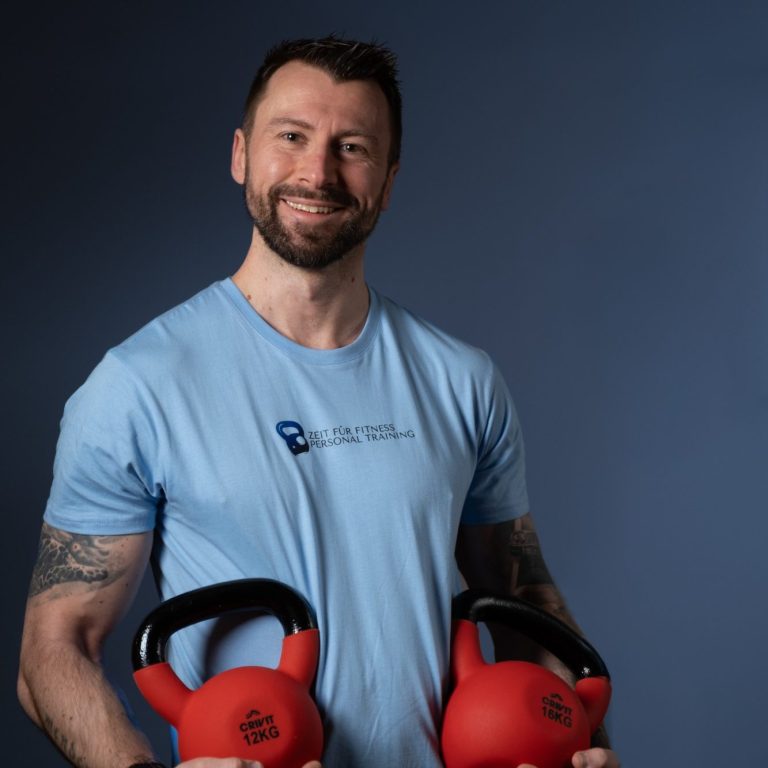 Personal Fitness Training Mann mit kurzer Frisur, hält zwei rote Kettlebells und lächelt freundlich.