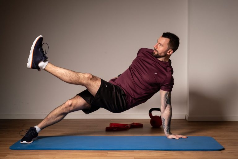 Bodyweight Training Mann in Sportkleidung führt eine seitliche Planke auf einer Yogamatte aus.