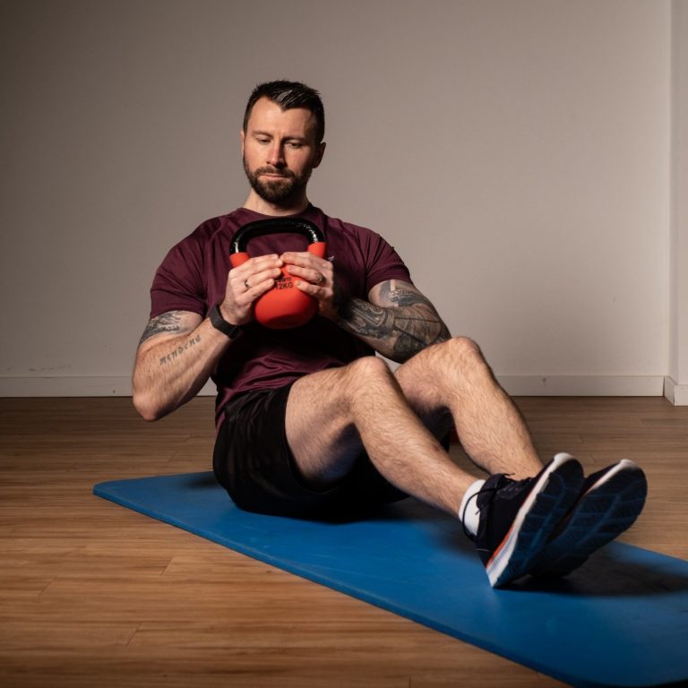 Kettlebelltraining Mann sitzt auf einer Matte, hält eine Kettlebell und führt eine Übung aus.