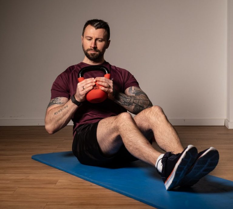 Kettlebell Training Mann sitzt auf einer Matte, hält eine Kettlebell und bereitet sich auf das Training vor.