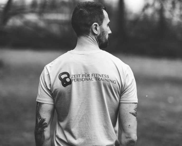 Schwarz-weiß Bild von einem Mann von hinten mit dem T-Shirt-Aufdruck "Zeit für Fitness - Personal Training" Schwarz-weiß Bild von einem Mann von hinten mit dem T-Shirt-Aufdruck "Zeit für Fitness - Personal Training"